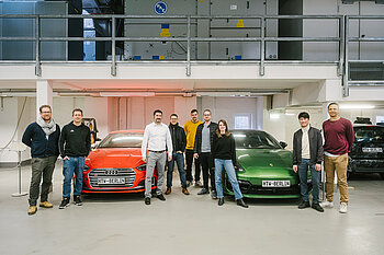 Gruppe von Studierenden mit Professor vor zwei Autos